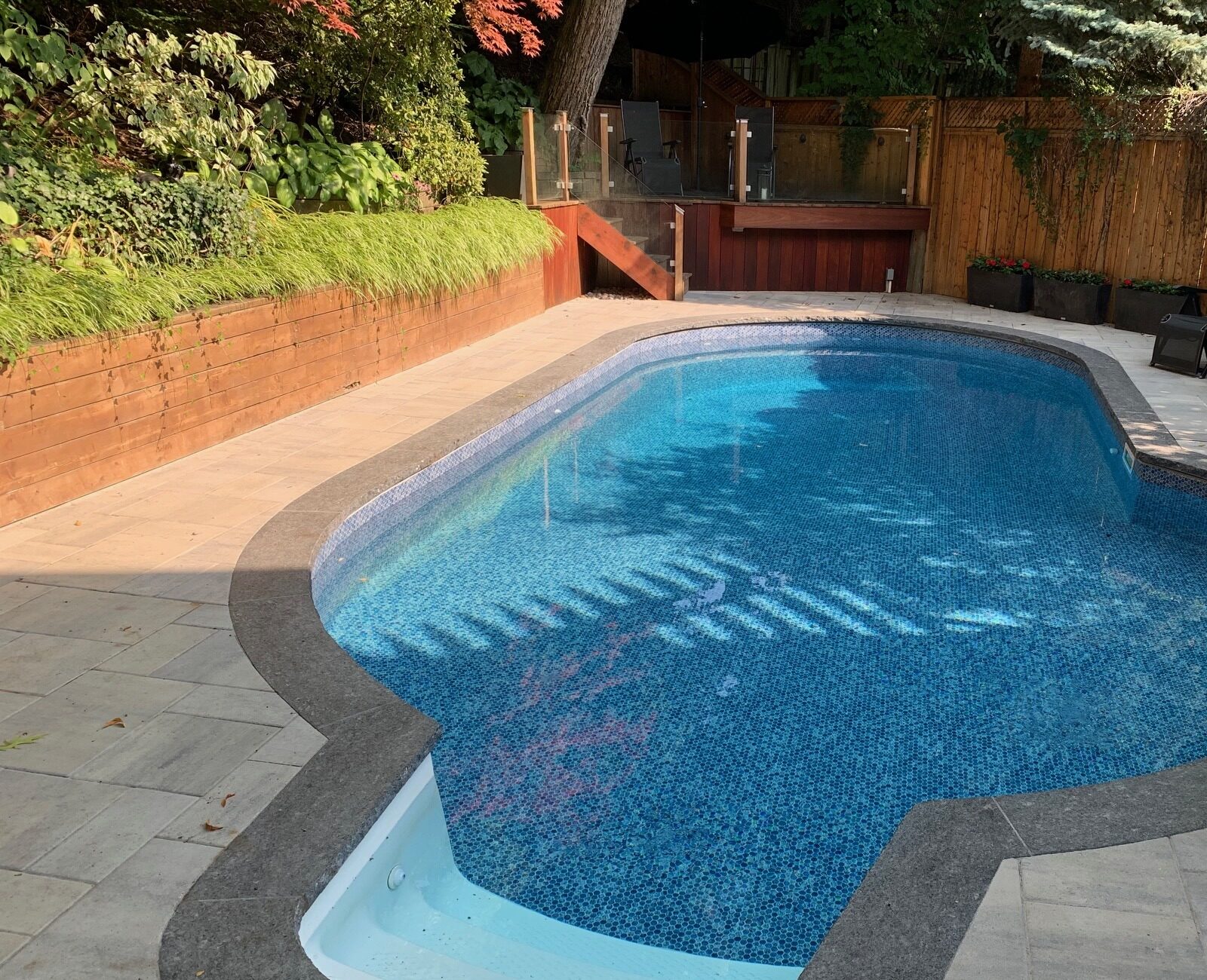 A serene backyard features a kidney-shaped pool surrounded by greenery, lounge chairs, and a wooden deck, creating a tranquil outdoor setting.