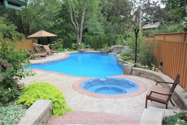 Backyard scene featuring a swimming pool and hot tub surrounded by patio chairs, trees, and a wooden fence, offering a serene, private setting.