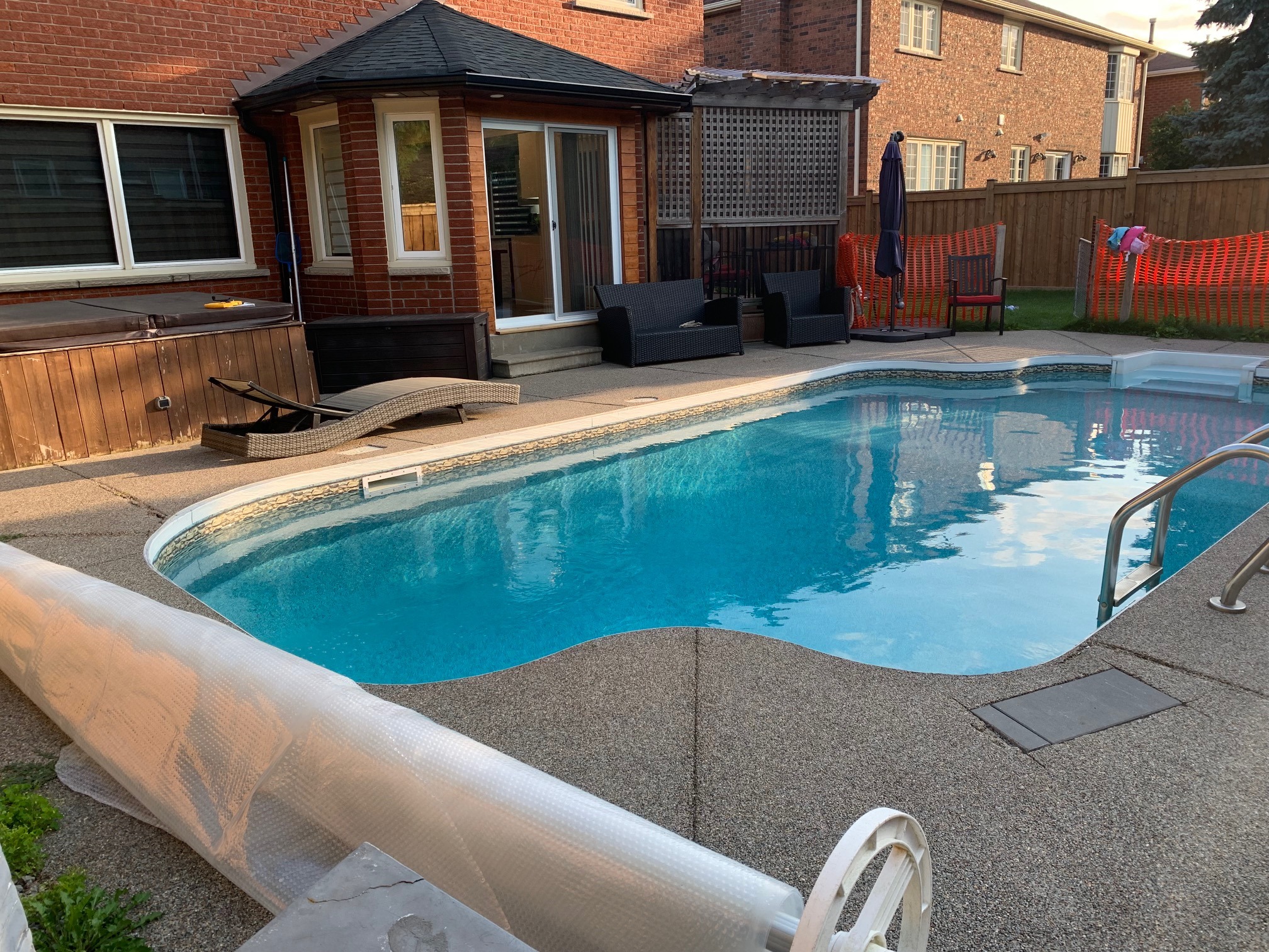 A backyard with a swimming pool, surrounded by patio furniture, brick house, and fencing, under a clear sky.