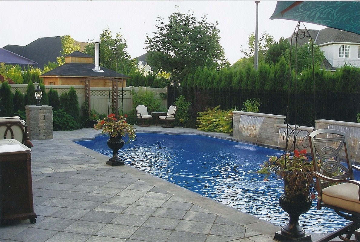 A backyard with a blue swimming pool, patio seating, lush greenery, and a small wooden structure, exuding tranquility and relaxation.